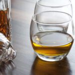 Glass of scotch whiskey alongside an open decanter on a bar counter or table with additional empty glasses